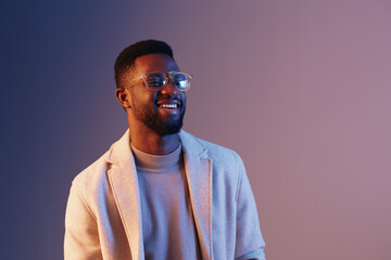 Smiling young African man wearing glasses in a stylish beige outfit against a soft gradient background, showcasing modern fashion and confidence
