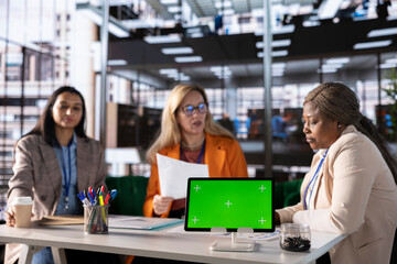Fototapeta premium Diverse group of female colleagues ensuring goals achievement next to chroma key display, believing in equal rights and women empowerment. Powerful businesswomen work with resilience.