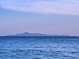 Distant island silhouette with wind turbines against blue sea and sky, calm seascape with mountain outline. Environmental conservation.
