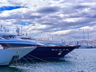 Modern luxury yachts docked in a marina with cloudy sky and distant mountains