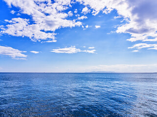 Tranquil blue sea under a bright sky with scattered white clouds stretching to the horizon