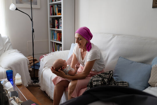 Grandmother with cancer holding newborn grandchild on sofa