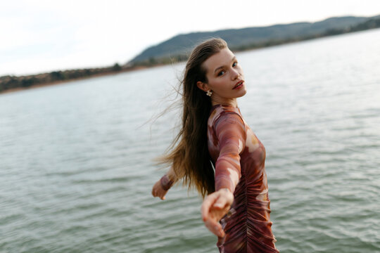 Calm woman with stretched arms near lake