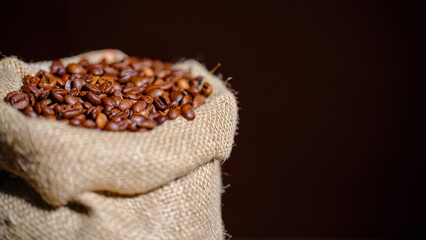A rustic burlap sack brimming with freshly roasted coffee beans, captured against a dark background, highlighting the natural beauty and inviting aroma of the beans.