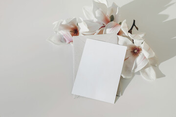 Spring styled stock photo. Blooming magnolia tree branch in sunlight. Vertical blank greeting card, invitation mockup, craft envelope. Feminine wedding stationery on white table background. Flatlay © tabitazn