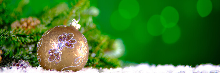 A glittery Christmas ornament with floral patterns atop a snowy branch, set against a vivid green...