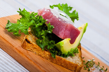 Image of tasty sandwich with raw tuna, avocado and greens at plate