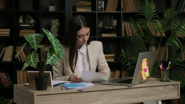 Female IT programmer analyzes a task she has to complete. Woman in classic suit at work in a modern and comfortable office thinks about how to complete a complicated program