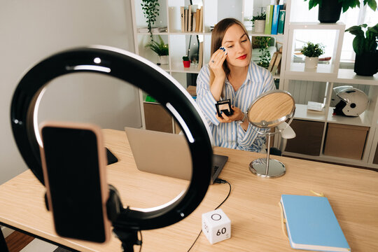 Woman applying face powder while preparing for video recording