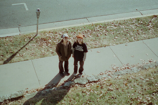 Two Twins Stand on a Sidewalk in Fall