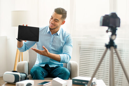 Arab guy vlogger making video review of innovative tablet pc, using camera at home, mockup on touch pad screen. Popular influencer sharing info about new tech product with followers online