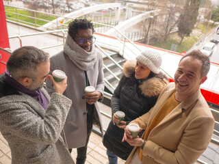 Four office workers on a coffee break in a busy business district. One Black male, a woman, and two Hispanic individuals are standing together. Only one of them, a Hispanic man, looks directly at the