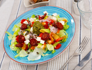 Delicious fresh vegetable salad with feta, chorizo, avocado and pesto sauce served on plate