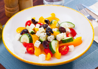 Fresh colorful Greek salad (horiatiki salad) served with feta cheese on white plate..