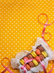 colorful macaroons cakes packed in a box with ribbon on a yellow polka dot background, space for text