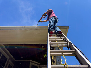 Man on ladder Pressure washer on porch of home 