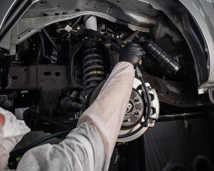 An auto mechanic applies anti-corrosion mastic to the underbody of a car.