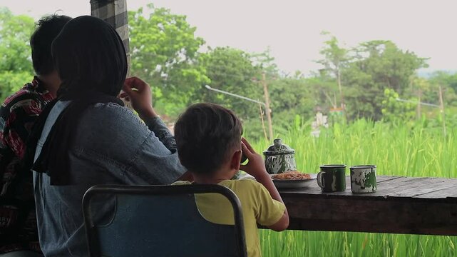 Asian muslim family doing chit chat talks while eating dinner, sitting on floor with low dining table, happy family