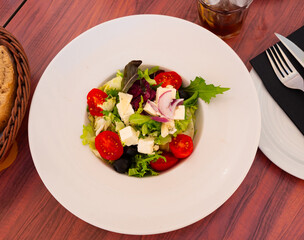 Crisp and refreshing colorful salad, perfect for dinner, with mix of lettuce, sliced tomatoes, onion, olives and cheese, served on white plate..