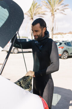 A guy taking his surfboard out of the trunk in a wetsuit