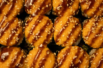  Top down photo of fresh rolls and sushi. Rolls garnished with brown sauce and sesame seeds.