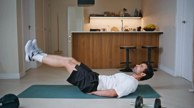 Fitness guy raising legs lying on sport mat at training exercises. Sportsman 