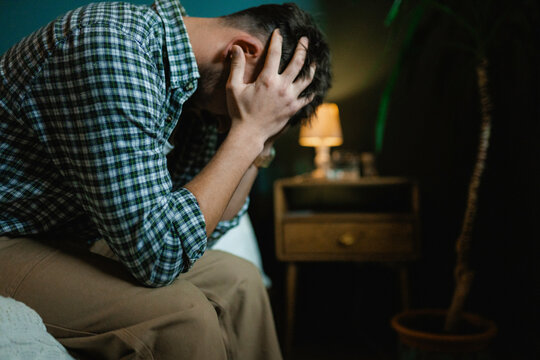 A man holds his head while sitting on the bed
