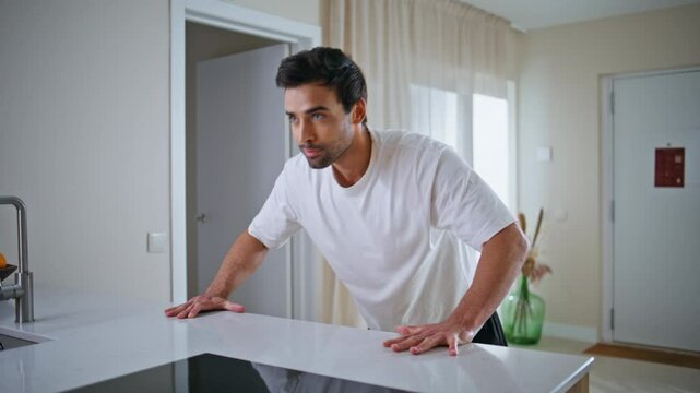 Determined man performing pushups on kitchen counter having home workout closeup