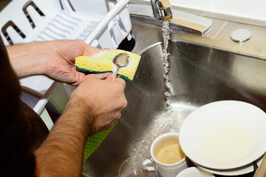 Anonymous young man washing a spoon by hand with a sponge
