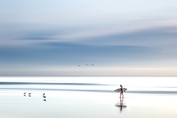 Lone surfer walking on California beach against a dramatic cloudscape