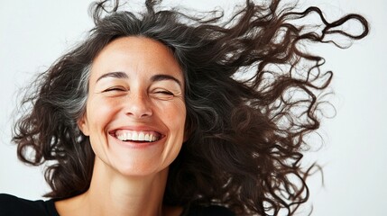 Joyful portrait showcasing genuine happiness with windswept curly dark hair flowing against white background, capturing authentic emotion and natural beauty in candid moment.