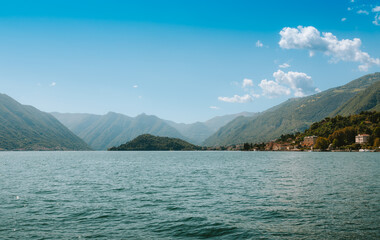 Panoramic view of Lake Como with mountains, blue sky and clouds reflecting in the calm water in...