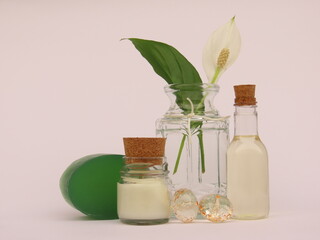 A small bottle of shower gel, a candle, a bar of soap and a peace lily flower and leaf in a vase on white background. A composition of self-care products for a moment of relaxation.