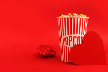 Bucket of popcorn and paper heart on red background. Valentine's Day celebration