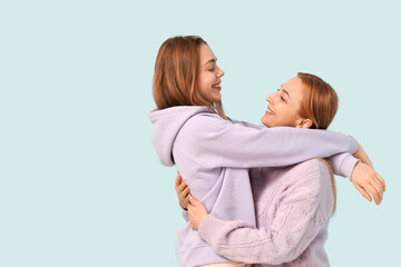 Beautiful young woman hugging her mother on blue background. International Hug Day