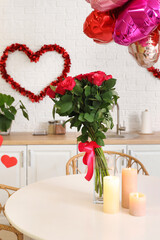 Bouquet of beautiful roses and burning candles on dining table in festive kitchen. Valentine's Day celebration