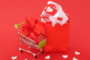 Small shopping cart with paper bag and gift boxes on red background. Valentine's Day celebration