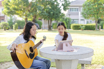Asian kid girl and friend learning online guitar lesson in the park, Friends playing guitar on...
