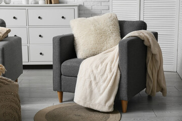 Grey armchair with soft cushion and blanket in living room