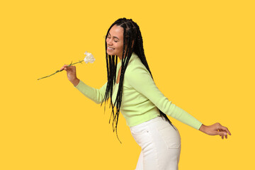 Beautiful young African-American woman with carnation flower on yellow background