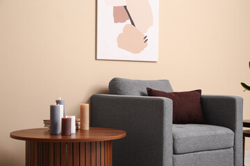 Interior of living room with armchair, painting and burning candles on table