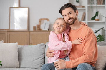 Cute little girl hugging her father while sitting on sofa at home. International Hug Day
