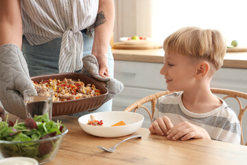 Young woman putting Fajita on table at dinner with her little son in kitchen