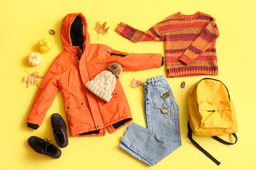 Composition with stylish children's clothes, shoes, accessories and fallen leaves on yellow...