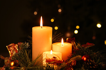 Composition with burning candles and Christmas wreath against decorated fir tree in evening, closeup
