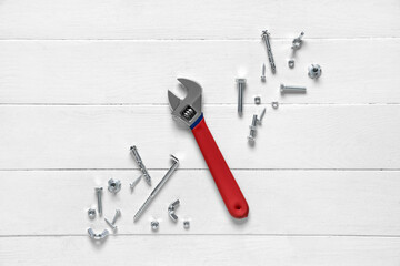 Adjustable wrench with tap bolts and chrome nuts on white wooden background