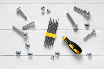 Tap bolts, chrome nuts and screwdriver bits on white wooden background