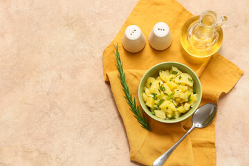 Bowl of tasty potato salad with green onion, rosemary and jug of oil on beige grunge background