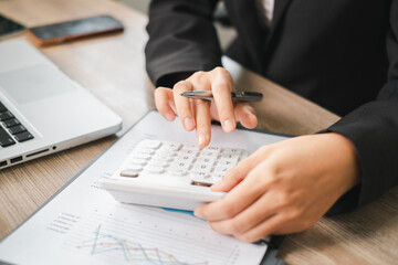 Business professional using a calculator and laptop to analyze financial data in an office...