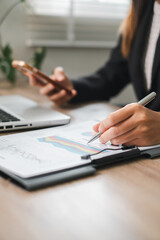 Fototapeta premium Professional woman reviewing charts and graphs at a desk, using a tablet and smartphone for business analysis.